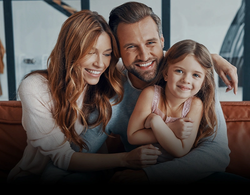 Happy family of three smiling together on couch in bright, modern home setting.
