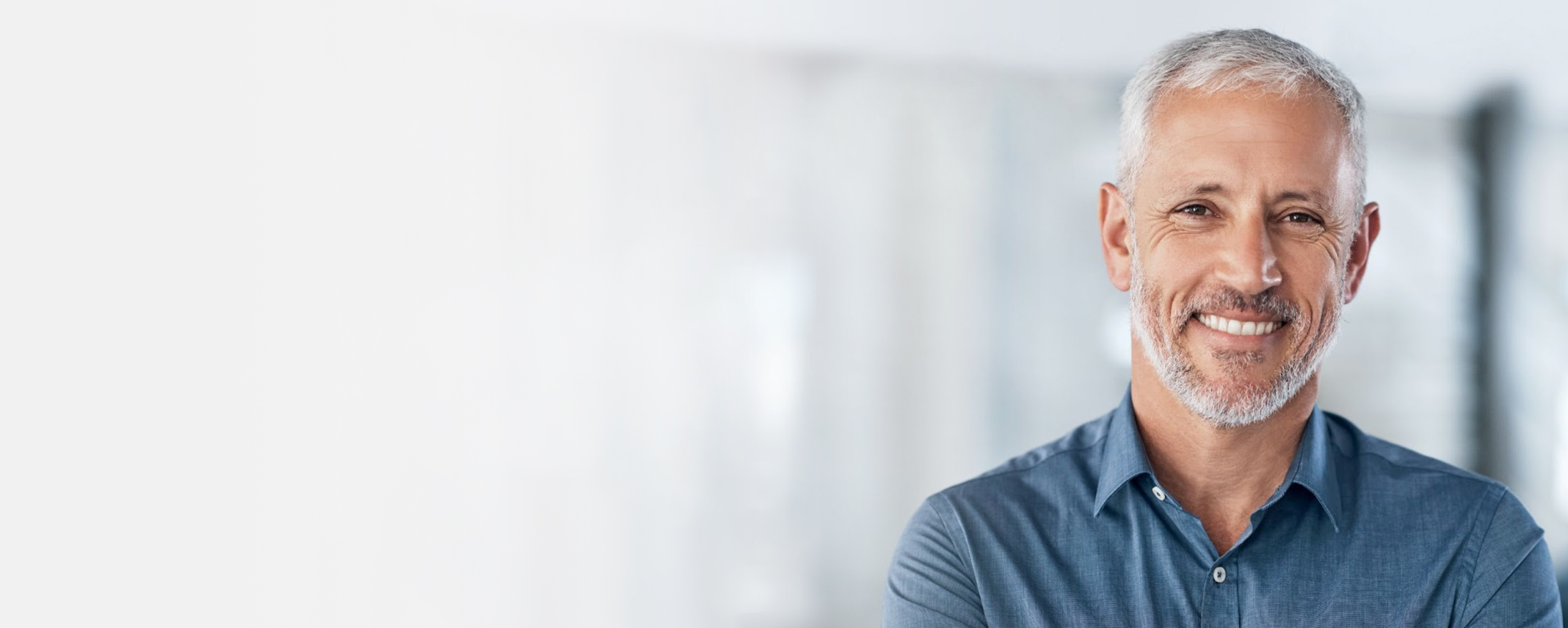 Smiling middle-aged man in blue shirt against blurred office background.