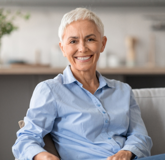 Smiling senior woman in light blue shirt seated in modern dental office interior