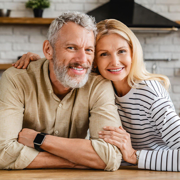 Smiling mature couple posing together at wooden table in modern home setting.