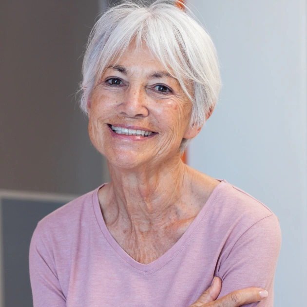 Smiling woman with white hair wearing pink shirt in professional dental office setting.